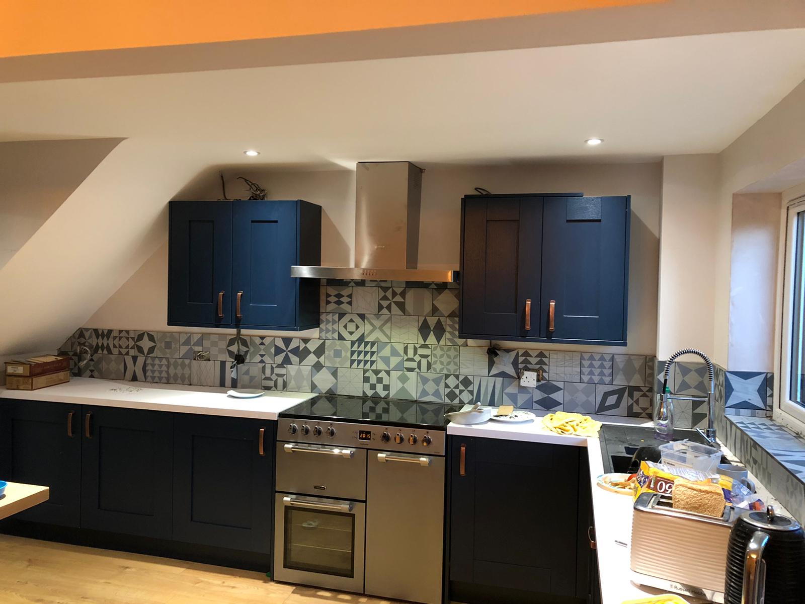 Navy shaker kitchen with copper handles, a stainless steel range cooker and patterned grey tiled splashback