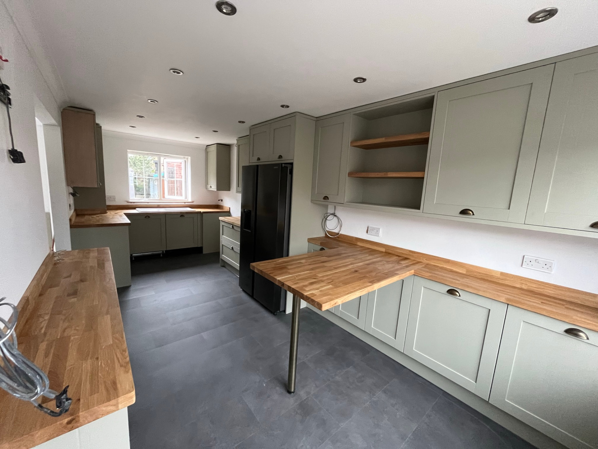 Sage green shaker kitchen with solid oak worktops, oak open shelving and a fitted oak breakfast bar