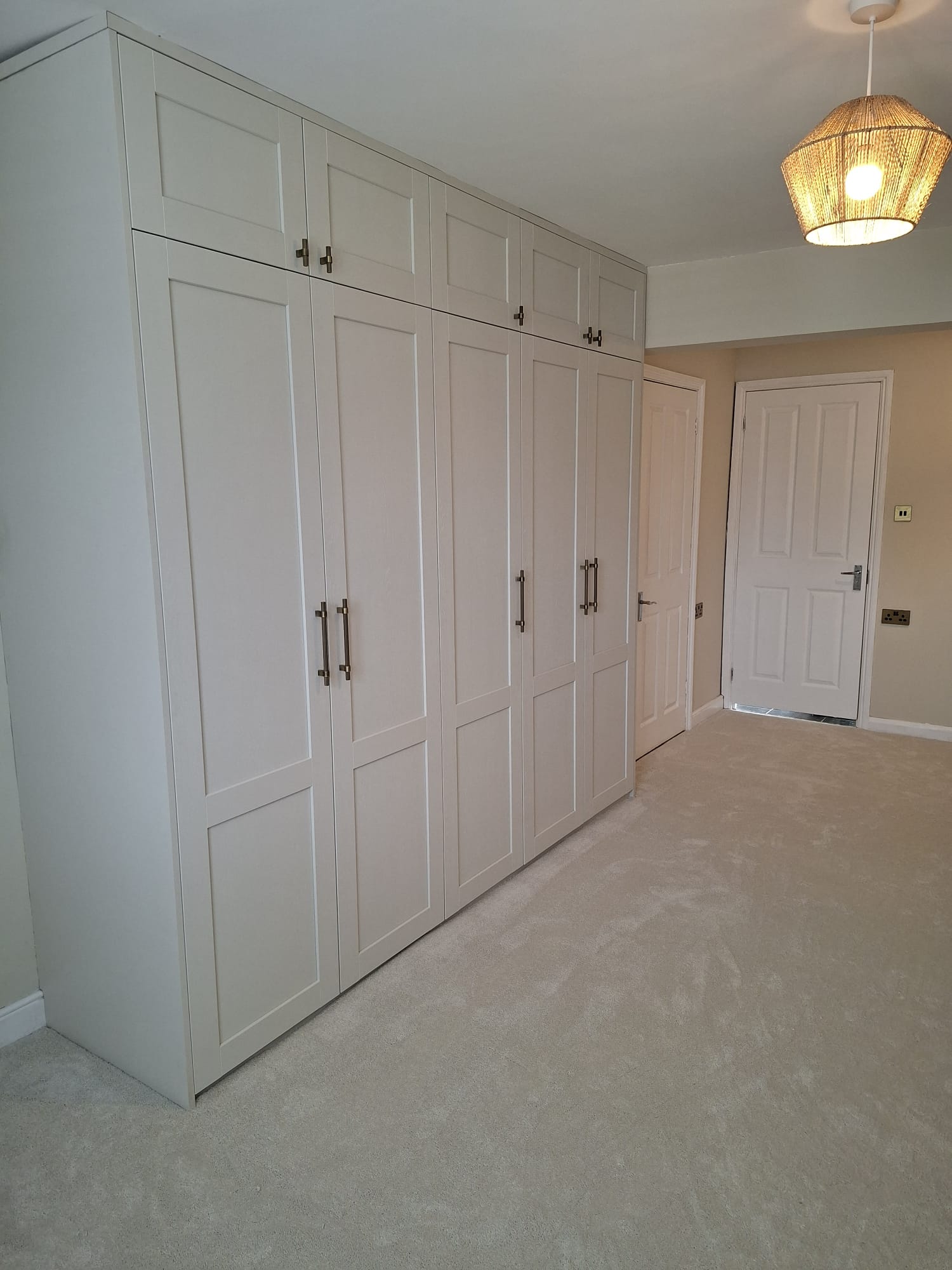 Floor-to-ceiling off-white shaker fitted wardrobes with aged brass handles in a bedroom
